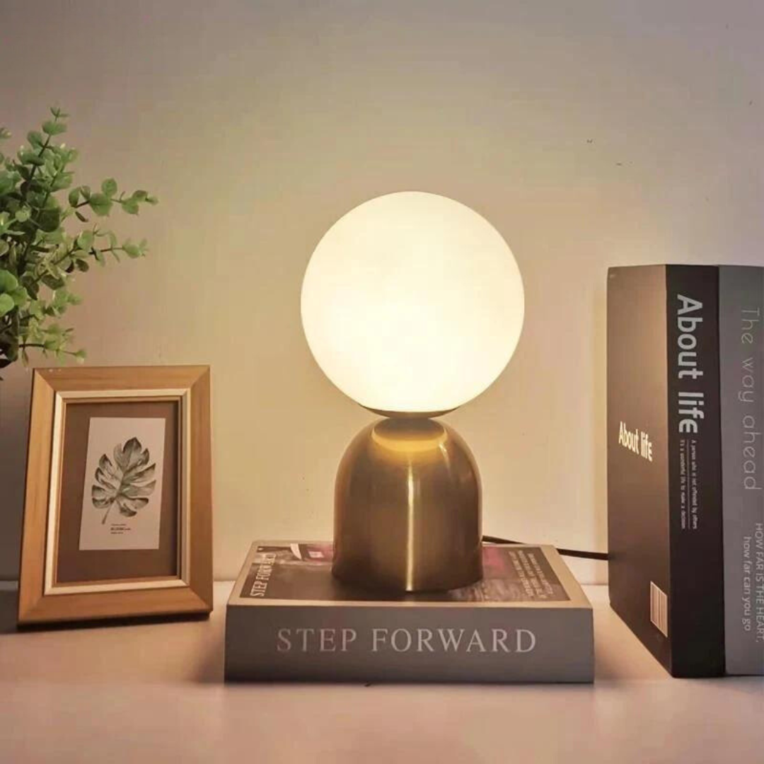Small Nordic Globe Table Lamp with brass base and round glass shade glowing on a table
