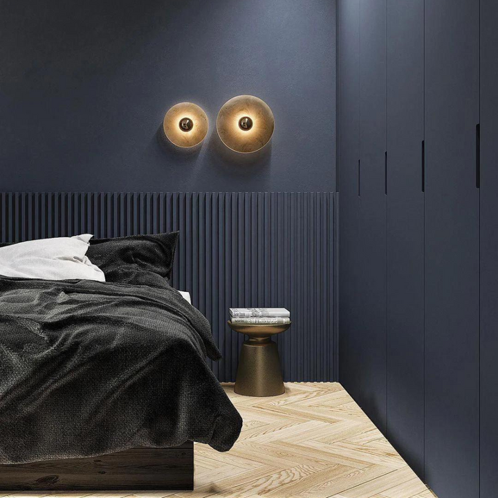 Warm illuminated round wall lamps installed above a bed in a modern bedroom.