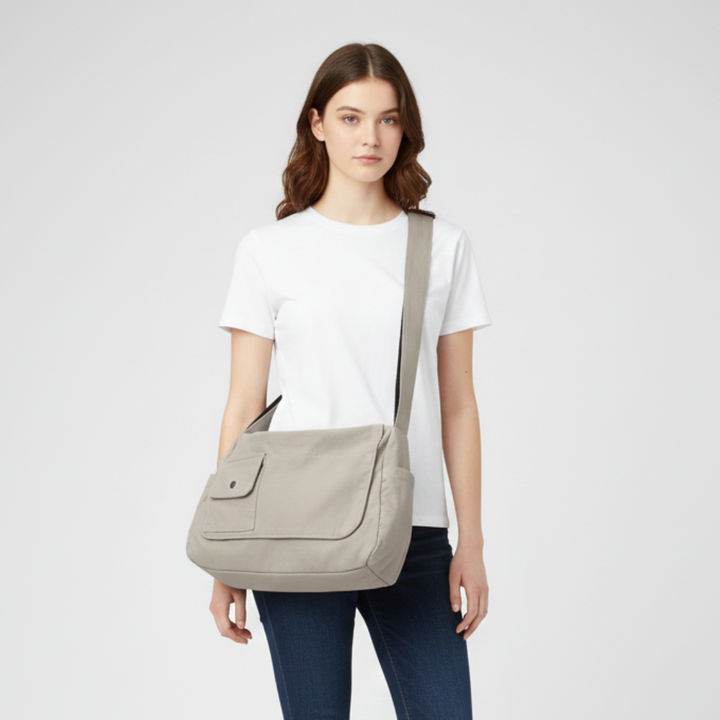 Woman wearing a grey canvas messenger bag against a neutral studio background