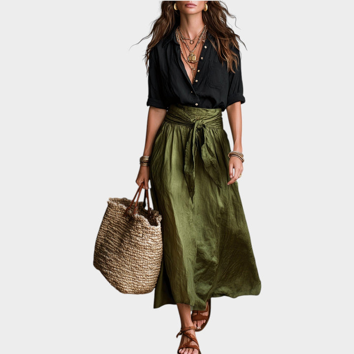 Woman wearing a black button-up shirt and green maxi skirt with a woven bag
