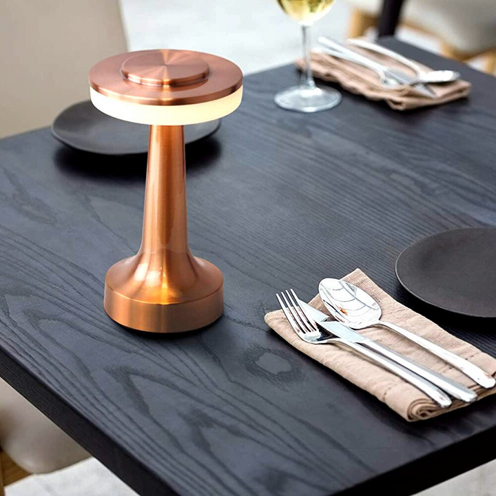 Rose gold cordless table lamp illuminating a dark dining table setup with cutlery and plates