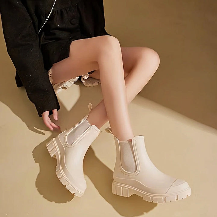 Model wearing beige waterproof rain boots sitting down with black coat