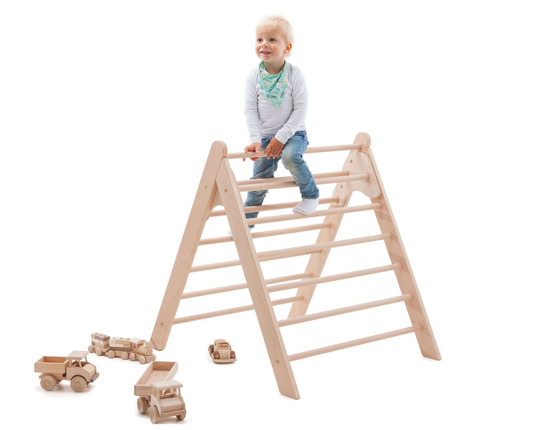 Toddler sitting on top of the wooden PlayBar climbing frame with toy cars on the floor