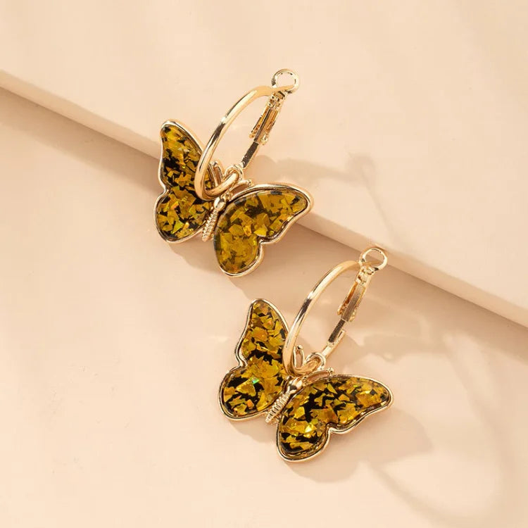 Gold hoop earrings featuring golden yellow crystal-filled butterfly charms resting on a neutral surface.