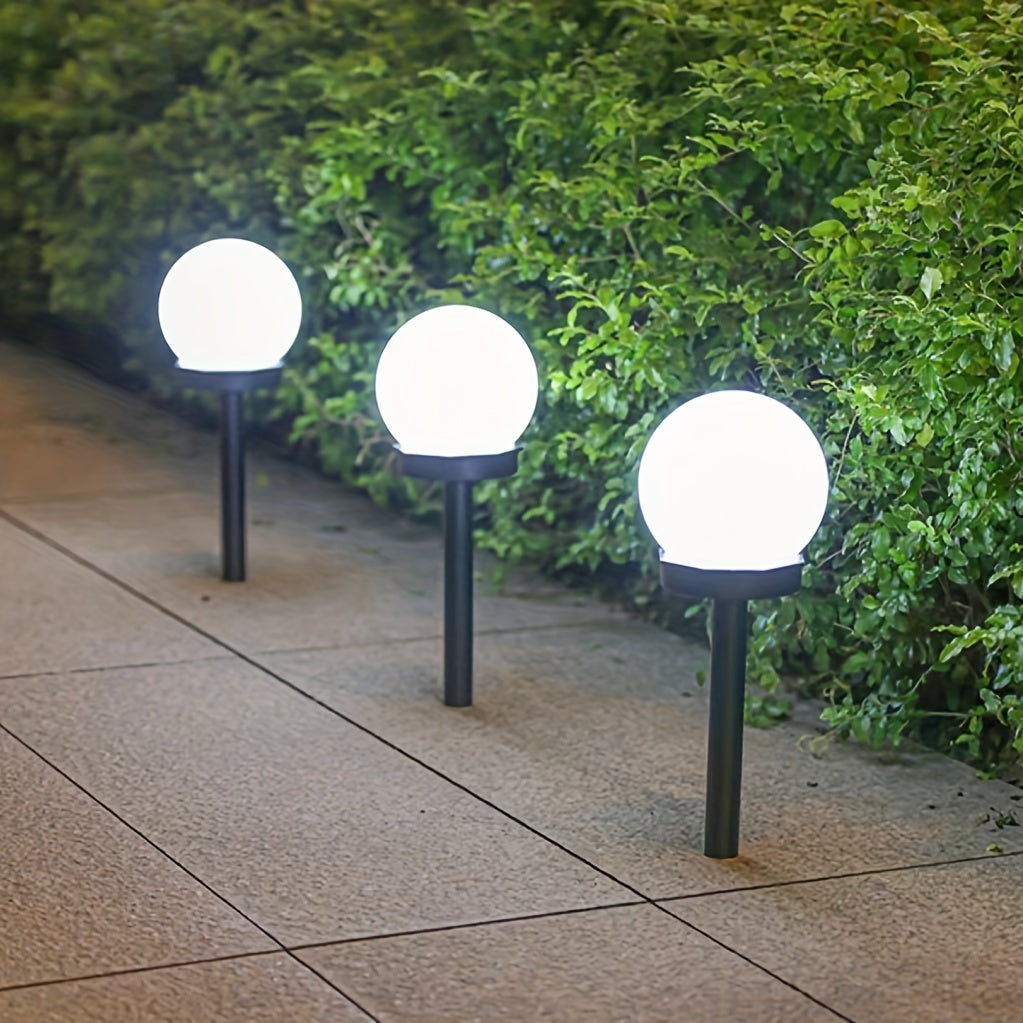Three spherical solar garden lights glowing softly along a backyard pathway at night.