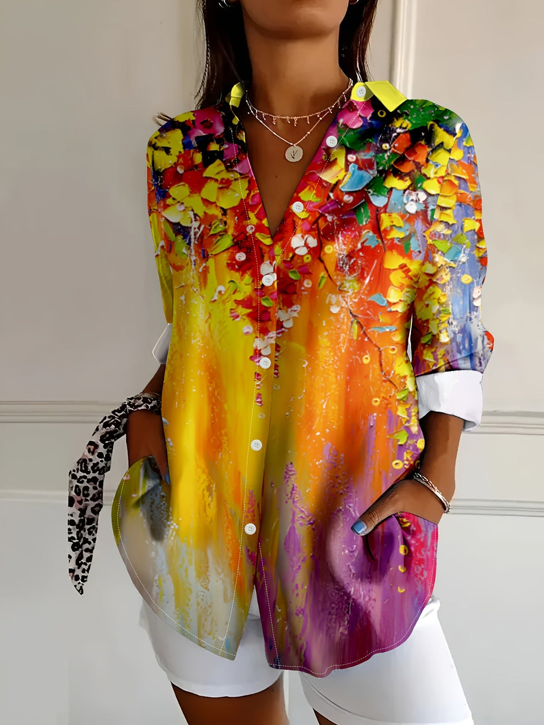 Front view of a woman wearing a vibrant floral print button-up blouse with white trousers.