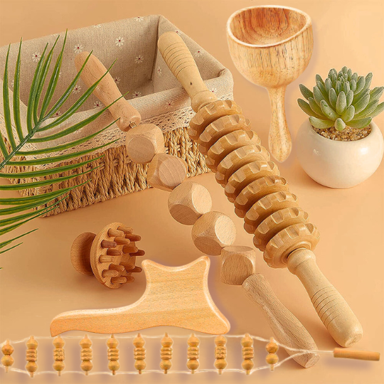 Collection of wood therapy massage tools arranged on a beige surface with a plant and basket