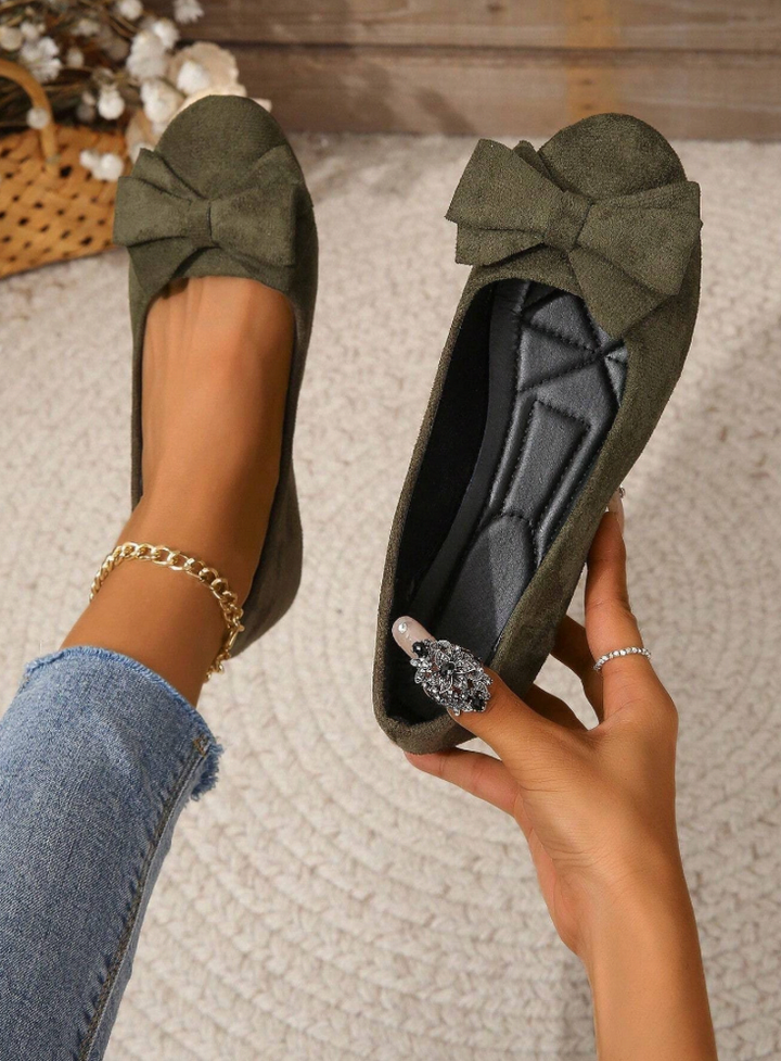 Dark green orthopaedic comfort flat shoe held in hand with decorative bow