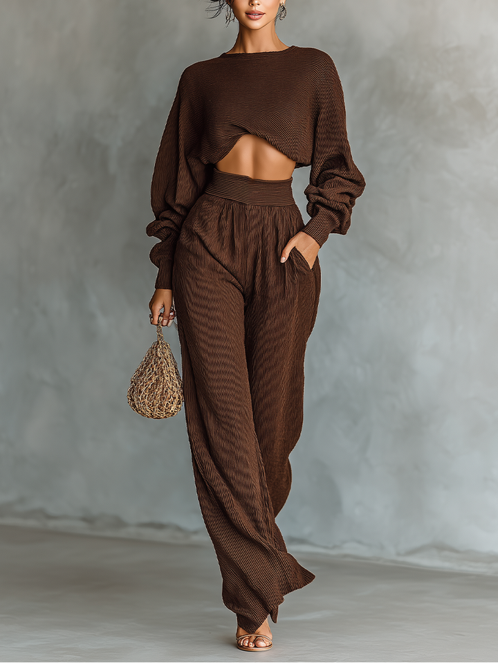 Model wearing a coffee brown knitted cropped top and wide-leg pants set holding a woven bag.