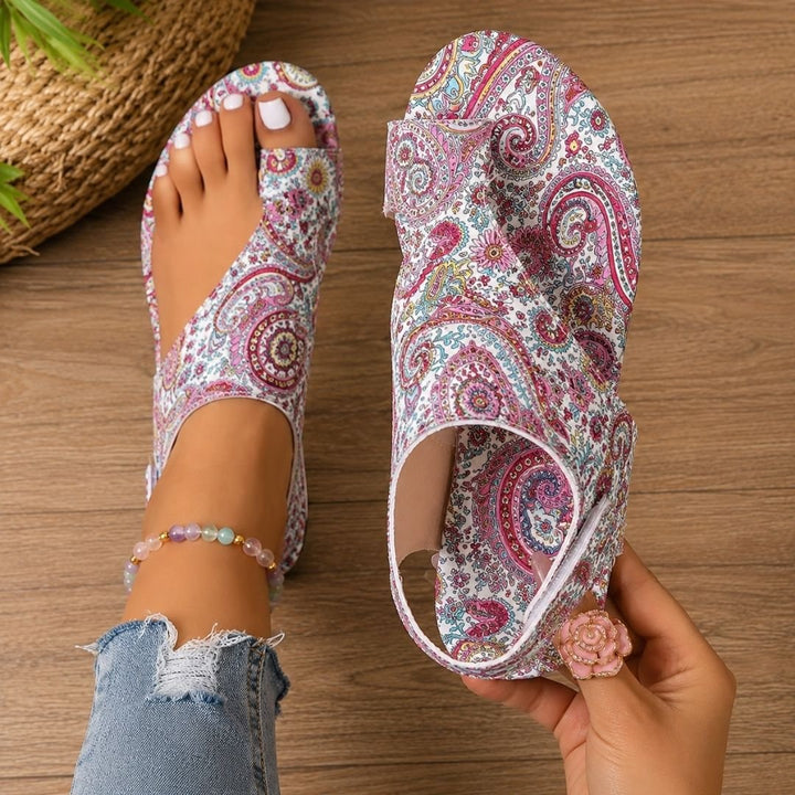 Woman holding pink patterned orthopaedic sandal displaying floral motif
