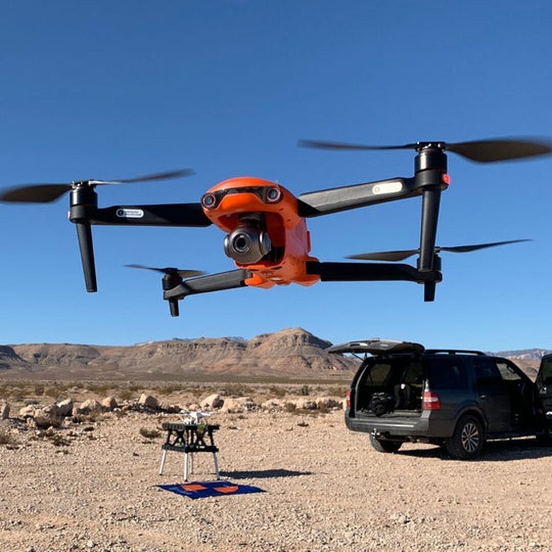Orange 4K UHD camera drone flying outdoors above rugged terrain under a blue sky