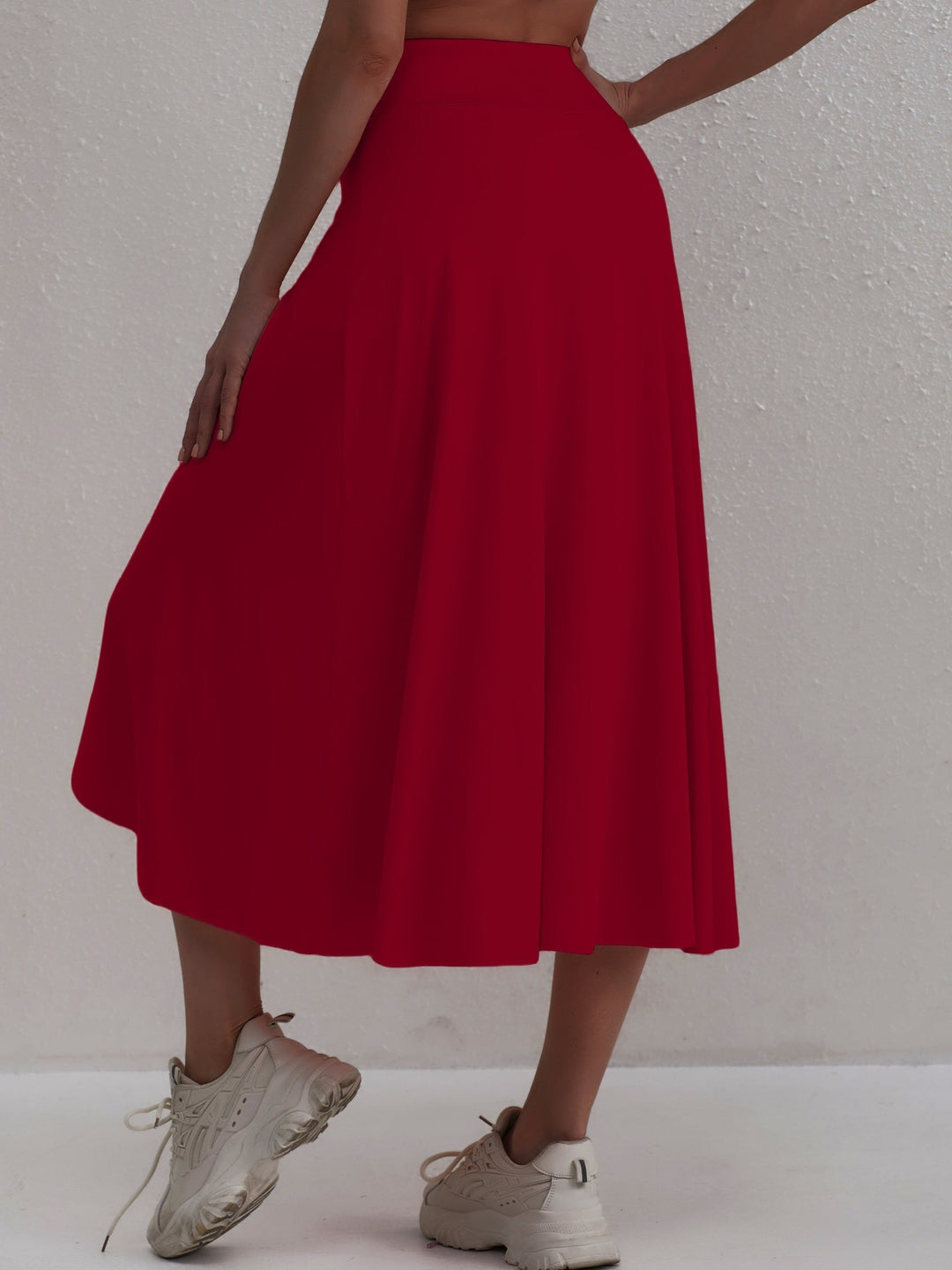 Back view of a woman wearing a red asymmetric athletic skirt with sneakers