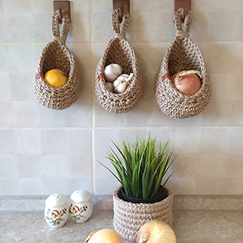 Three hanging woven baskets mounted on a tiled wall holding lemons, garlic, and an onion
