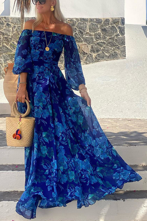 Woman wearing a blue floral off-shoulder maxi dress outdoors holding a woven bag