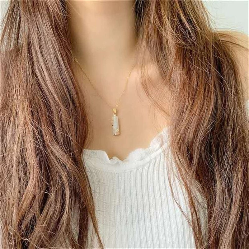 Model wearing a delicate jade pendant necklace against a white top