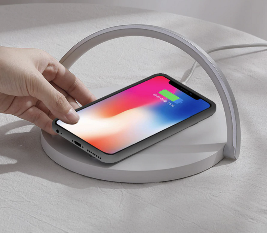 Hand placing a smartphone on the white wireless charging night lamp base