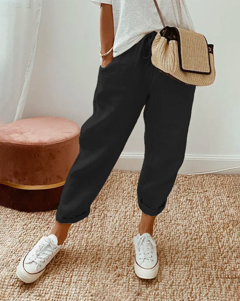 Woman wearing black high-waist casual trousers with white sneakers and a woven crossbody bag