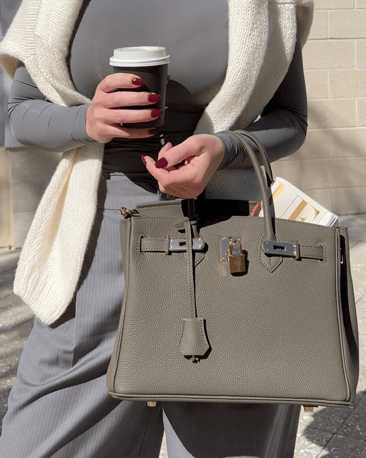 Woman holding gray Madelyn handbag and coffee cup on city street