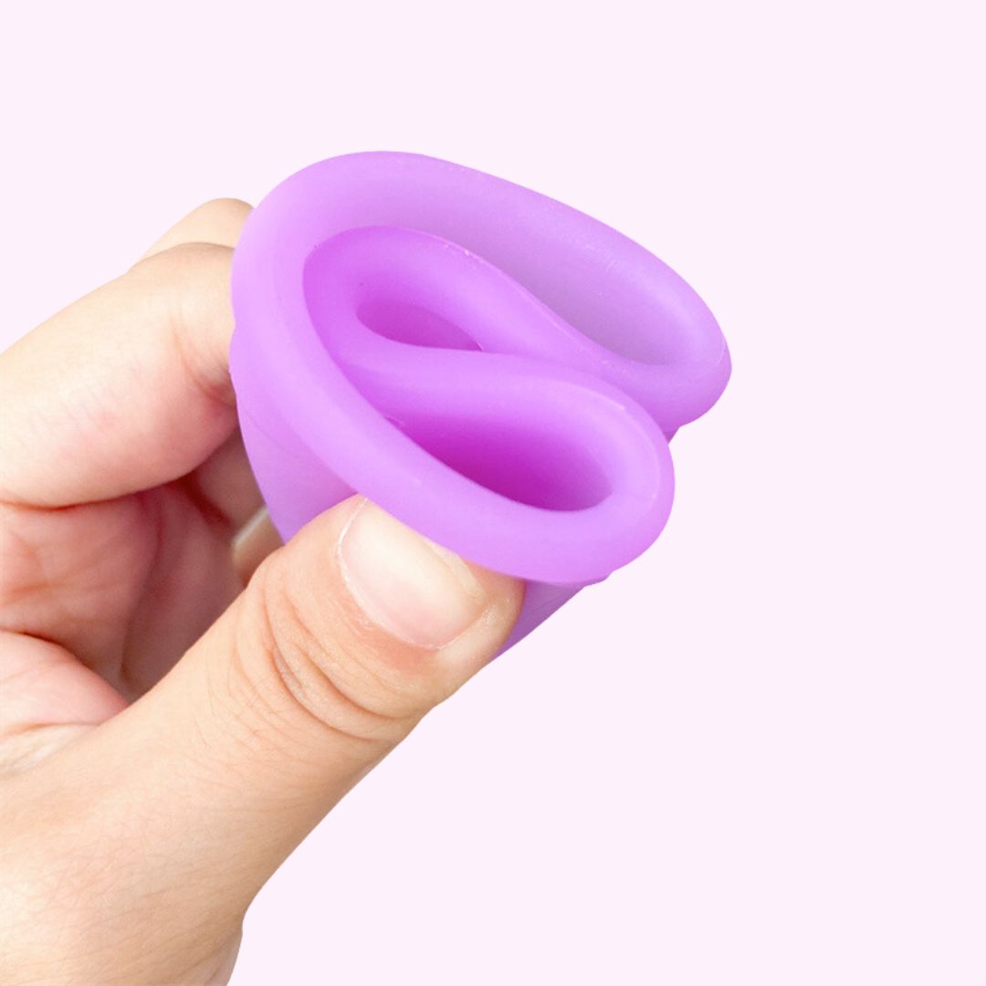 A hand demonstrating the flexible folding method of a purple menstrual cup