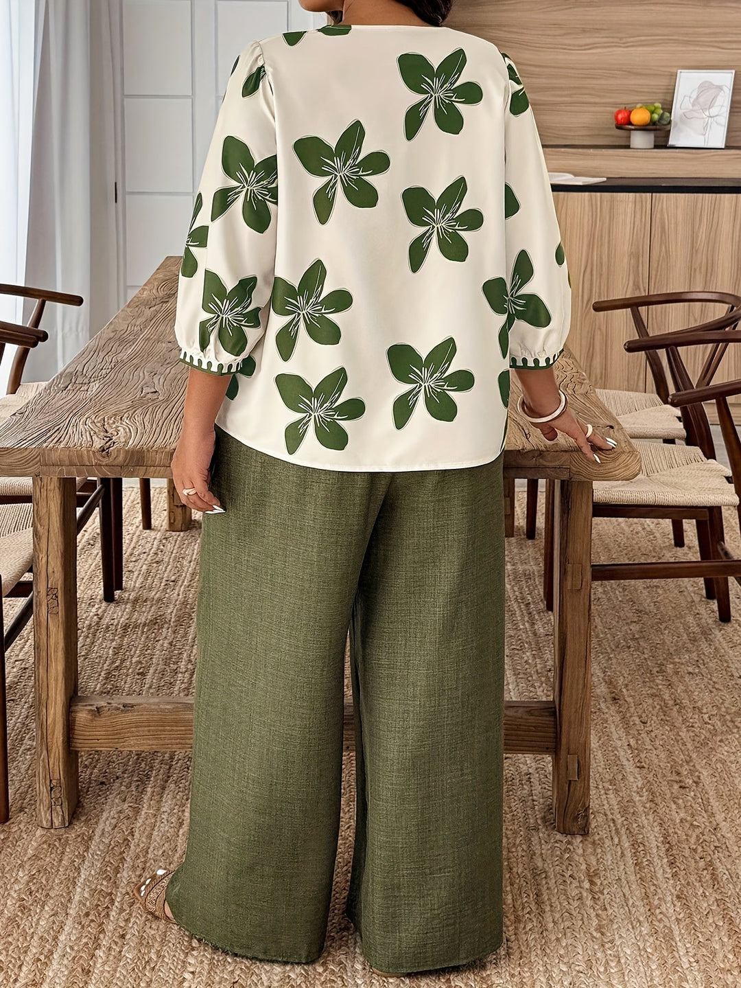 Back view of a woman wearing a green floral two-piece set with relaxed trousers and printed blouse.