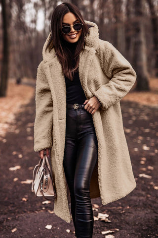 Woman wearing a beige hooded winter coat outdoors with sunglasses and a handbag