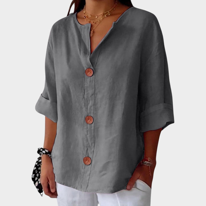 Woman wearing grey relaxed 3/4 sleeve button up blouse with white trousers