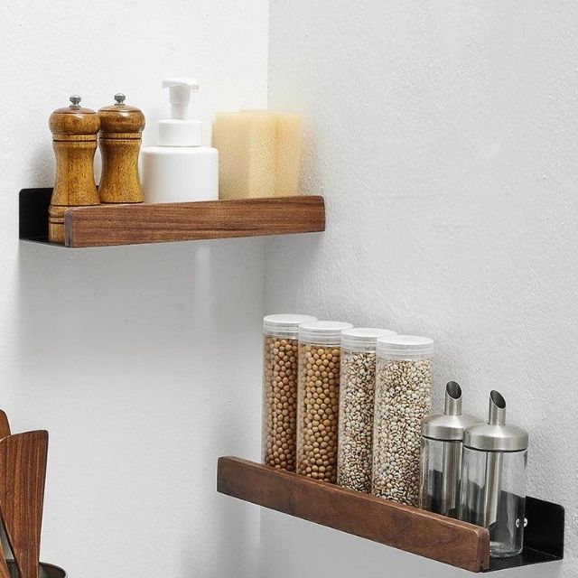 Brown solid wood bathroom shelf holding spice jars and bottles mounted on a white wall