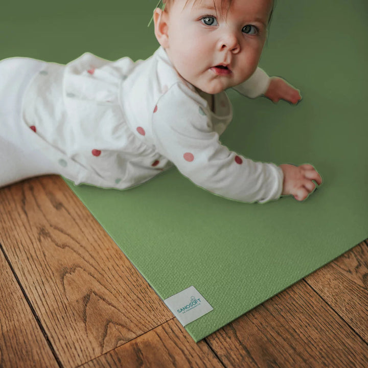 Baby crawling on a green EcoGrip foam play mat on wooden flooring