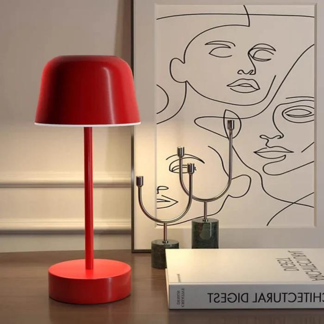 Red adjustable modern table lamp on a wooden desk next to artwork
