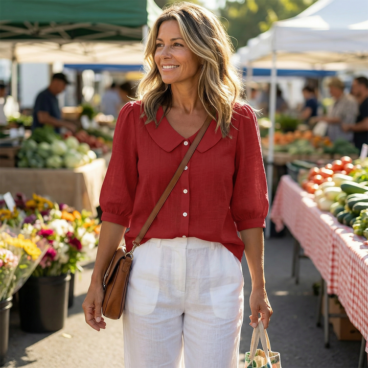 Woman walking at an outdoor market wearing a red button-up blouse and white trousers