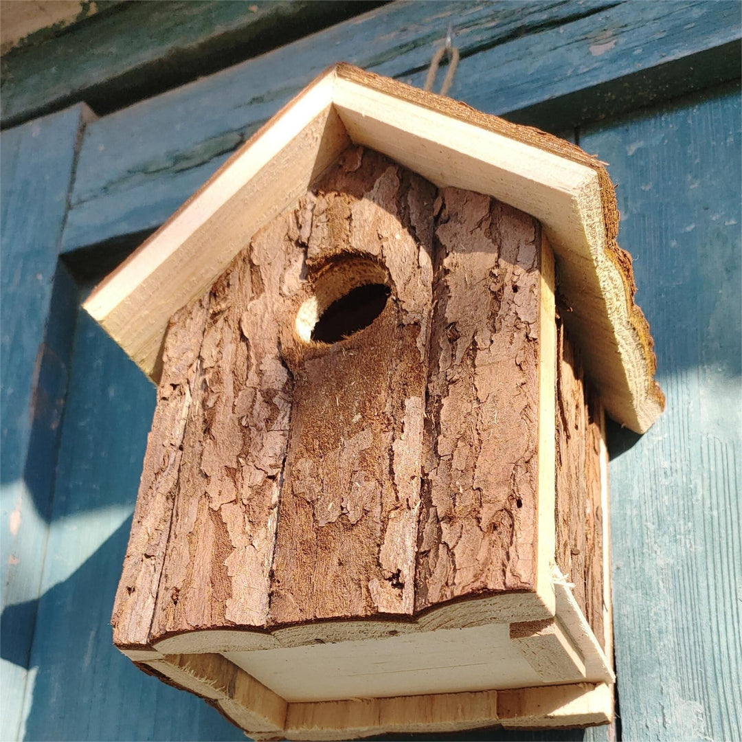 Close-up of rustic wooden bird house with bark finish hanging outdoors