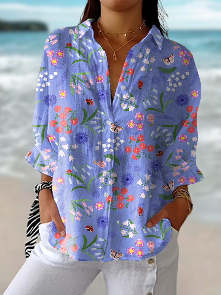 Woman wearing a purple floral print button-down blouse with pocket details by the beach