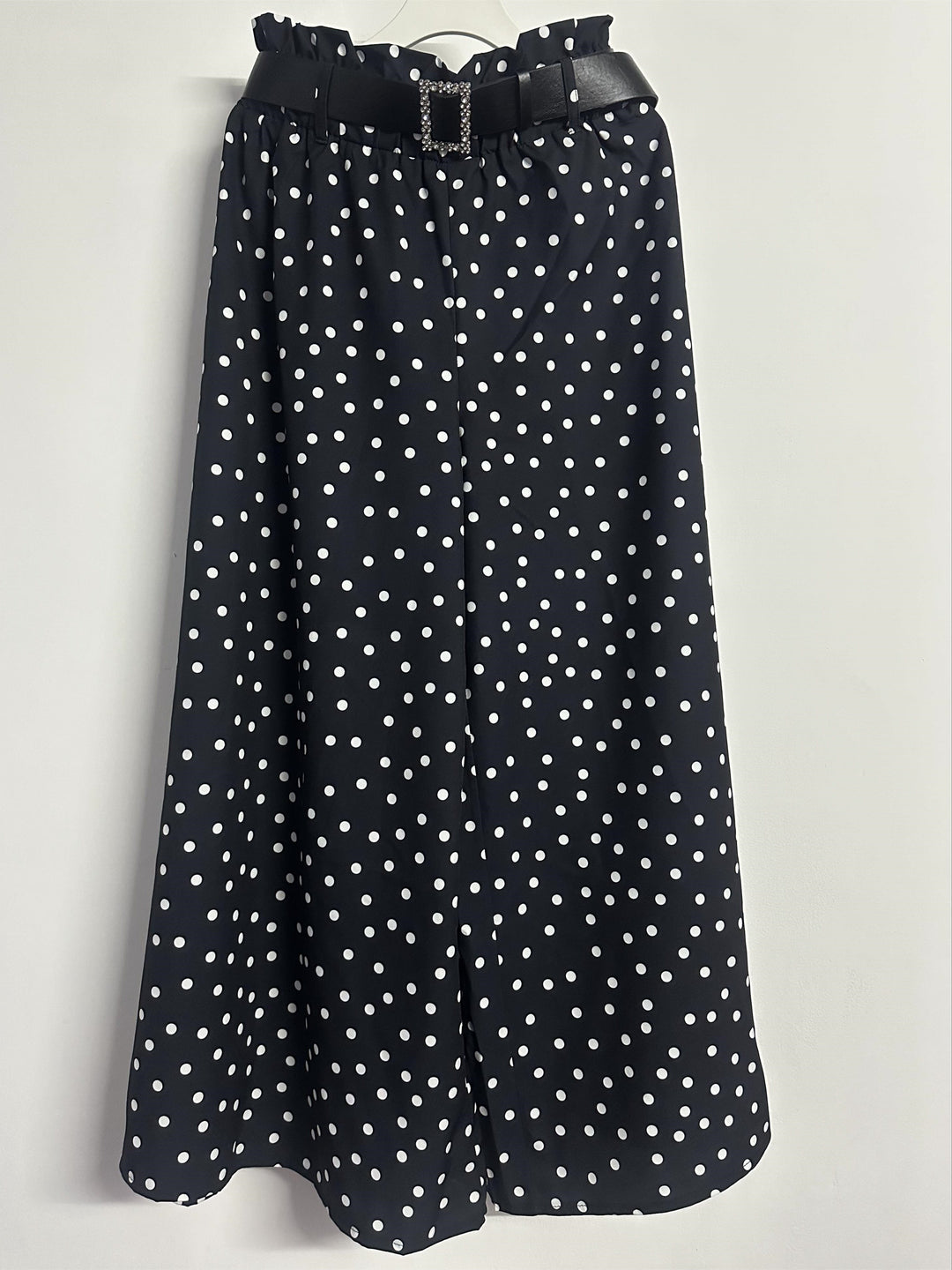 Front view of black and white polka dot wide-leg trousers hanging against a white wall