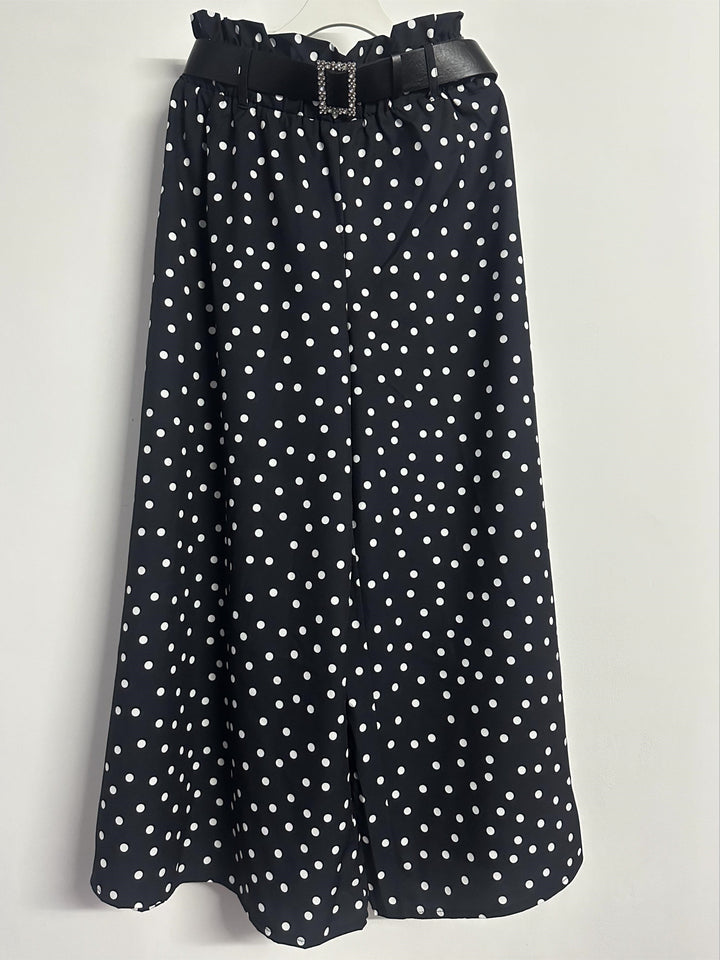 Front view of black and white polka dot wide-leg trousers hanging against a white wall
