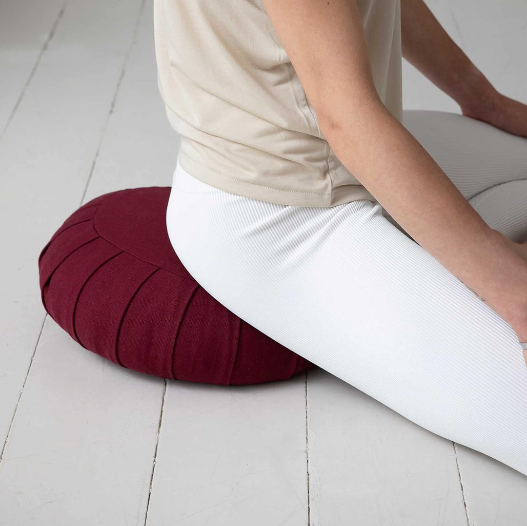 Person sitting cross-legged on a dark red ZenRest meditation cushion
