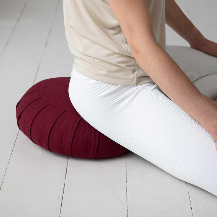 Person sitting cross-legged on a dark red ZenRest meditation cushion