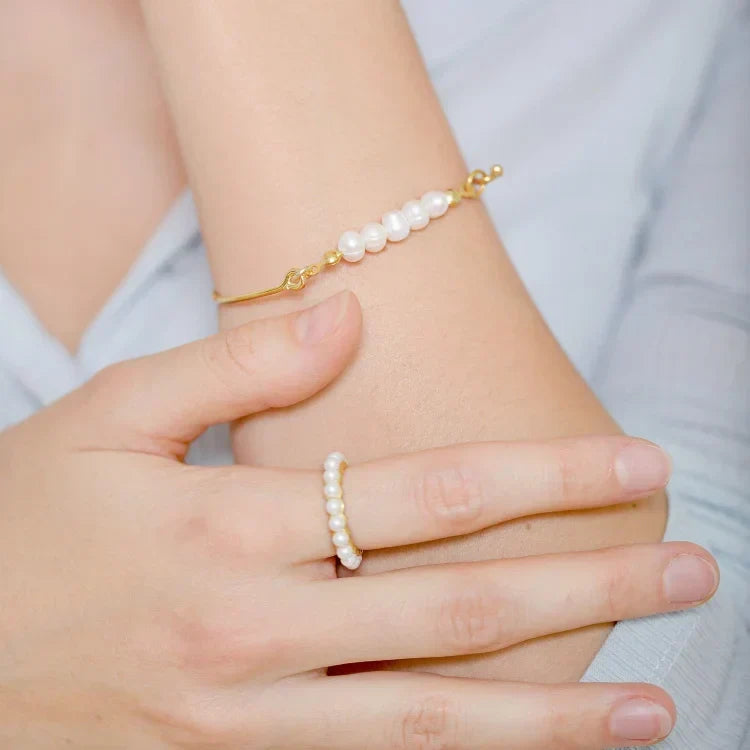 Woman wearing the Selina gold pearl bracelet and matching pearl ring on her arm and hand.