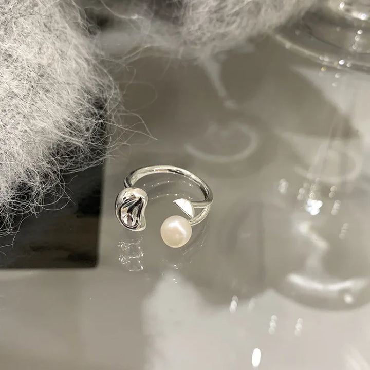 Detailed view of the open band pearl ring resting on a reflective tabletop surface.