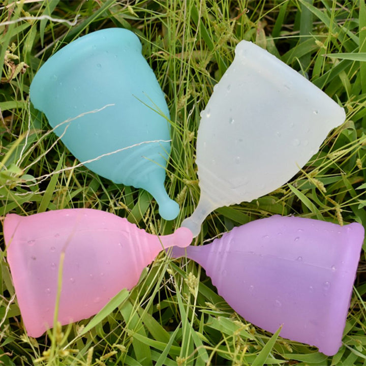Four silicone menstrual cups in different colors resting on green grass
