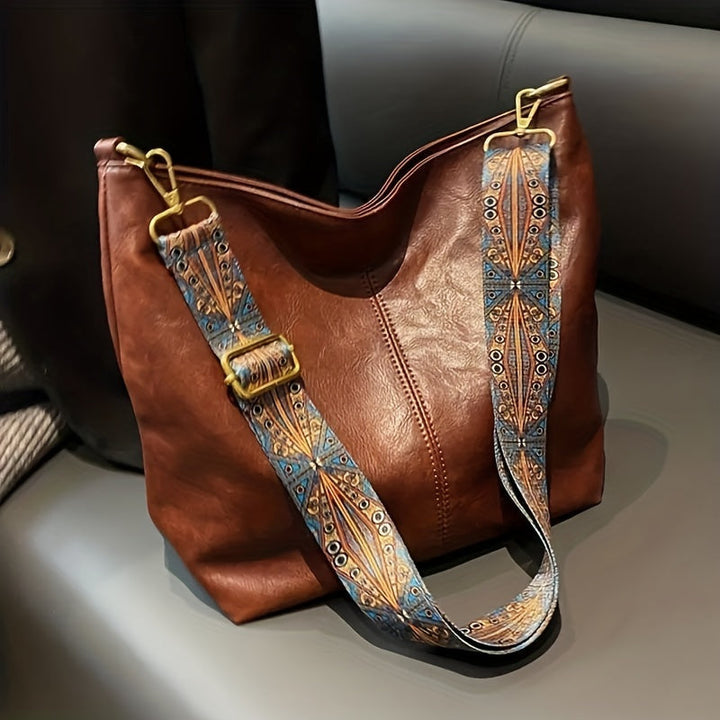 Close-up of brown geometric shoulder bag featuring an ornate wide strap