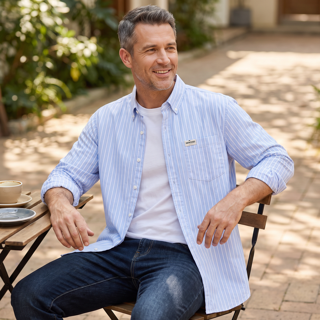 Man wearing light blue striped button-up shirt while sitting outdoors