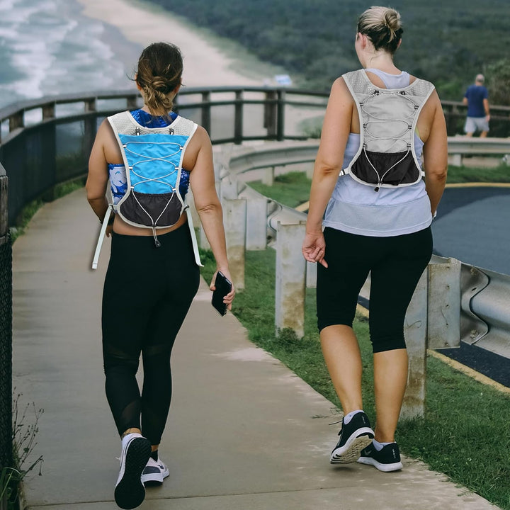Two runners walking outdoors wearing blue and grey hydration vests on a coastal path