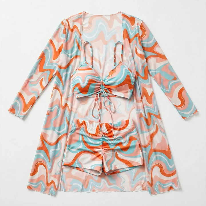 Flat lay of the orange swirl print three-piece bikini and sheer cover-up set