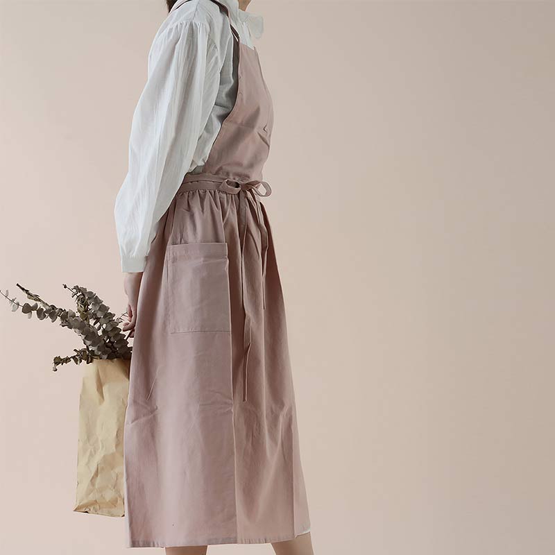 Side profile view of a woman wearing a pink kitchen apron with deep pockets