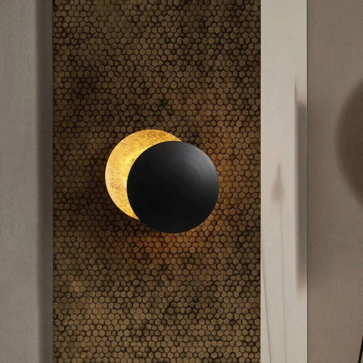 Black and gold modern moon wall lamp mounted on a patterned wall
