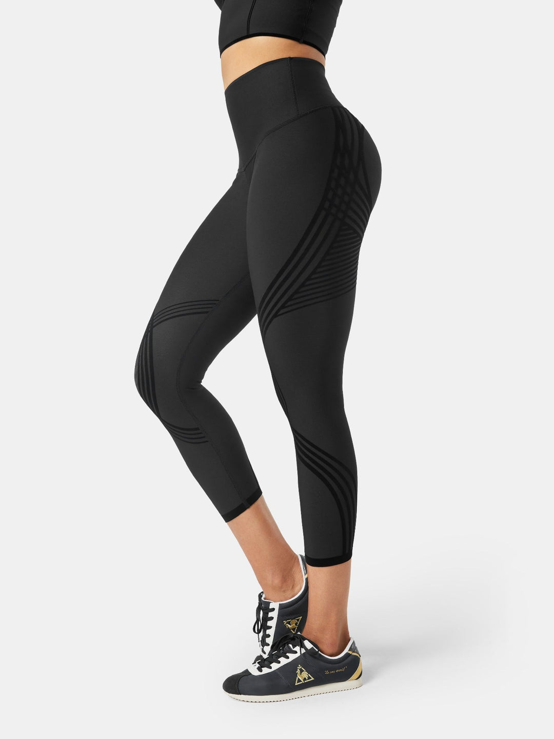 Side profile of a woman wearing black high-waisted 7/8 gym leggings with patterned panels