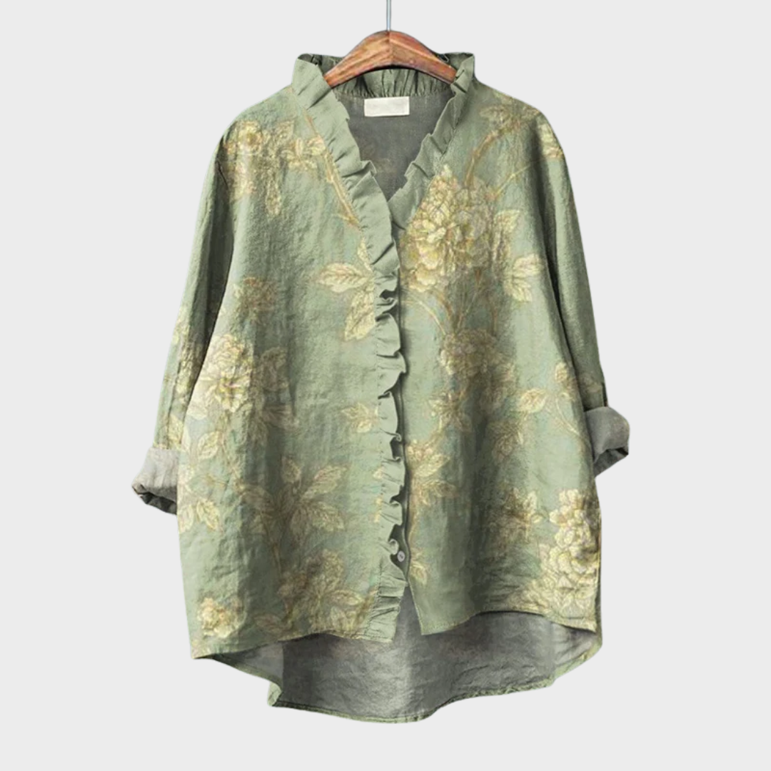 Women's elegant floral green summer blouse with ruffled collar hanging on a wooden hanger