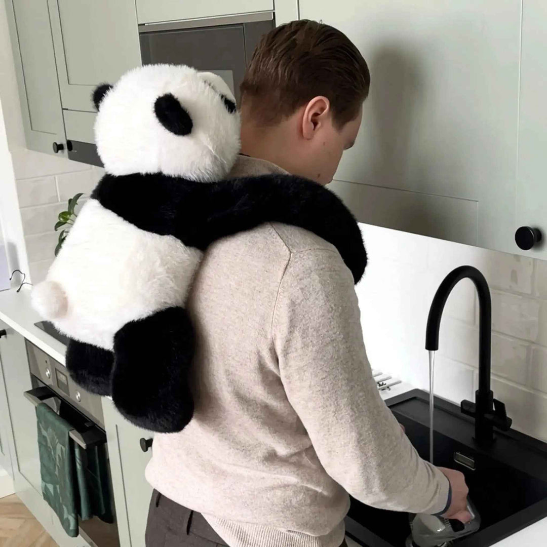 Man wearing the large weighted panda plush around his shoulders in a kitchen
