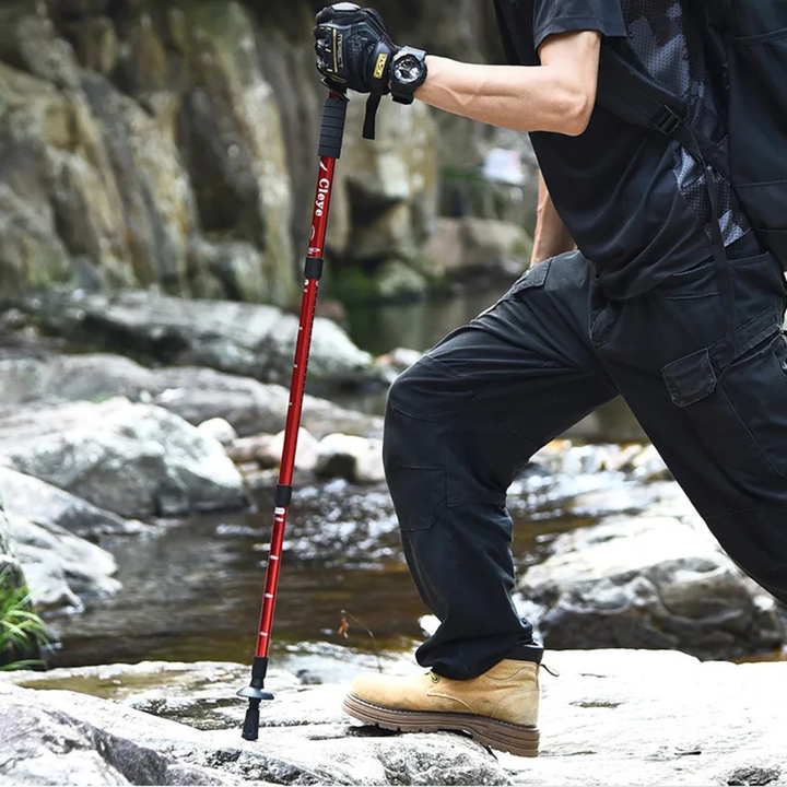 Hiker using a red collapsible aluminium trekking pole on rocky outdoor terrain