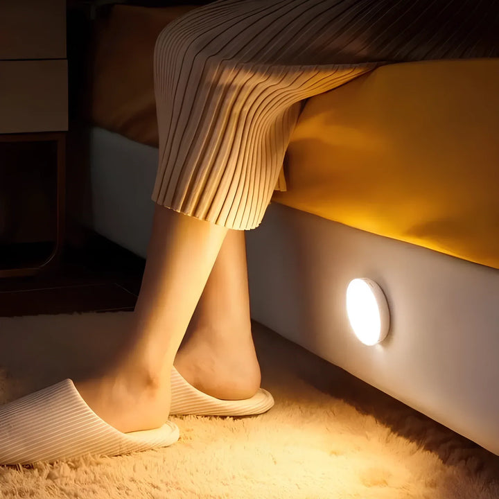 Compact LED motion light installed near a bed frame illuminating the floor